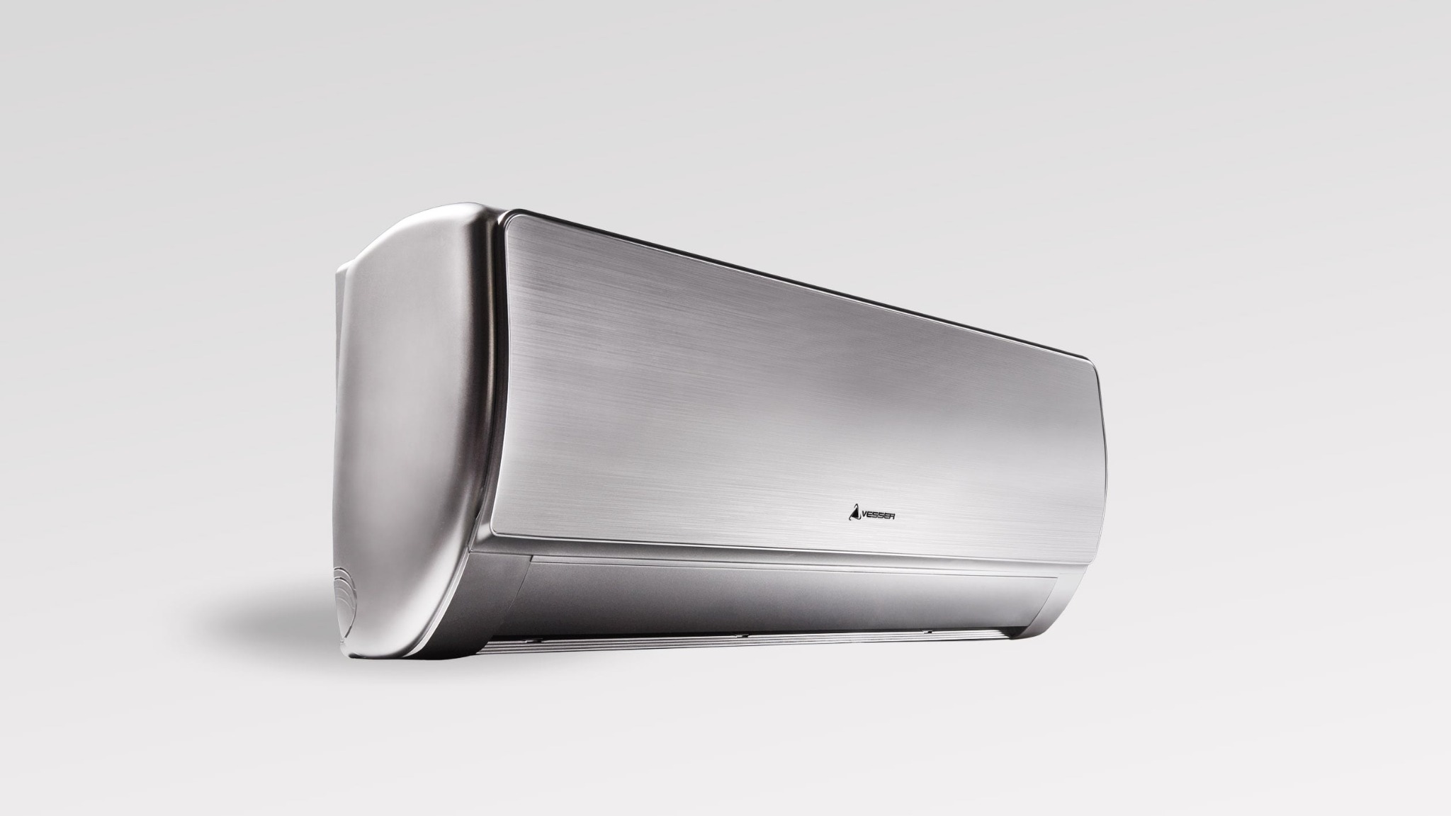 Nowoczesny, srebrny klimatyzator ścienny marki Vesser, ustawiony pod kątem na białym tle, eksponujący szczotkowaną fakturę obudowy i zaokrąglone krawędzie.