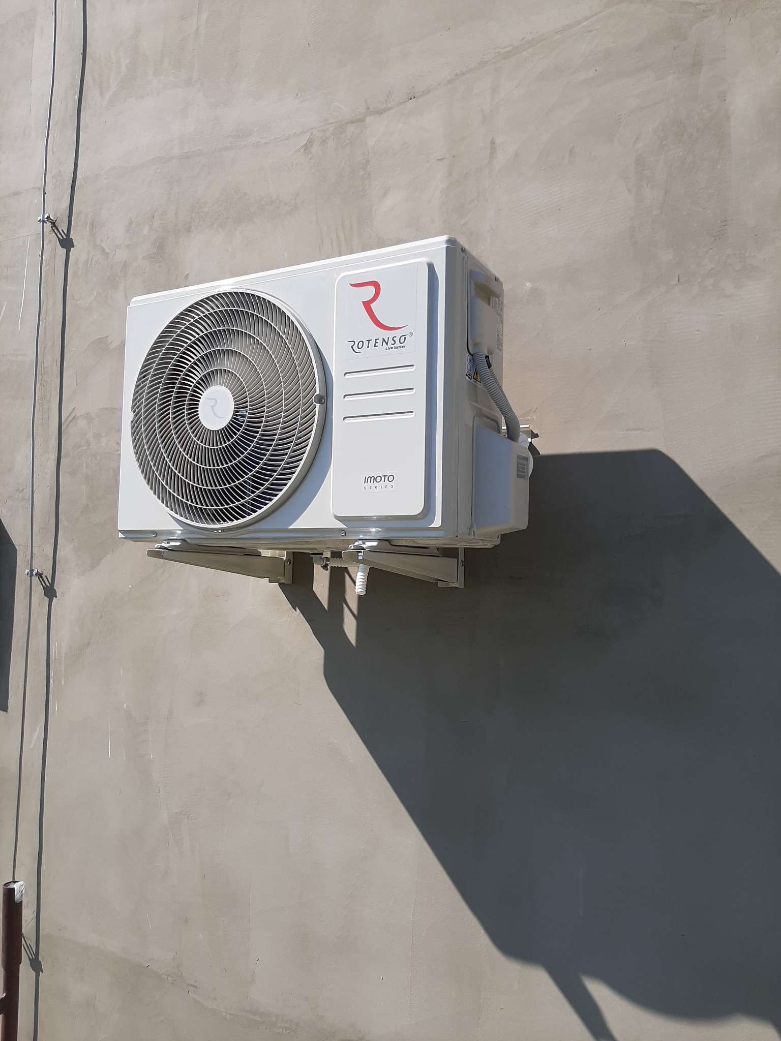 Biała jednostka zewnętrzna klimatyzatora Rotenso Imoto zamontowana na szarej ścianie budynku w Głogowie, widoczny cień urządzenia.