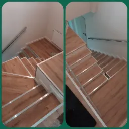 Schody wykończone panelami drewnopodobnymi z białymi listwami i metalowymi krawędziami antypoślizgowymi, widok z góry na dół, z fragmentem grzejnika i poręczy.