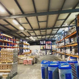 Wnętrze magazynu we Wrocławiu wypełnione materiałami budowlanymi, widoczne regały z wełną mineralną w rolkach i workach, drewno na paletach oraz inne materiały budowlane.