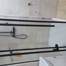 Zamontowana, szklana kabina prysznicowa z czarnymi profilami na tle beżowych płytek, widoczny brodzik i bateria prysznicowa.