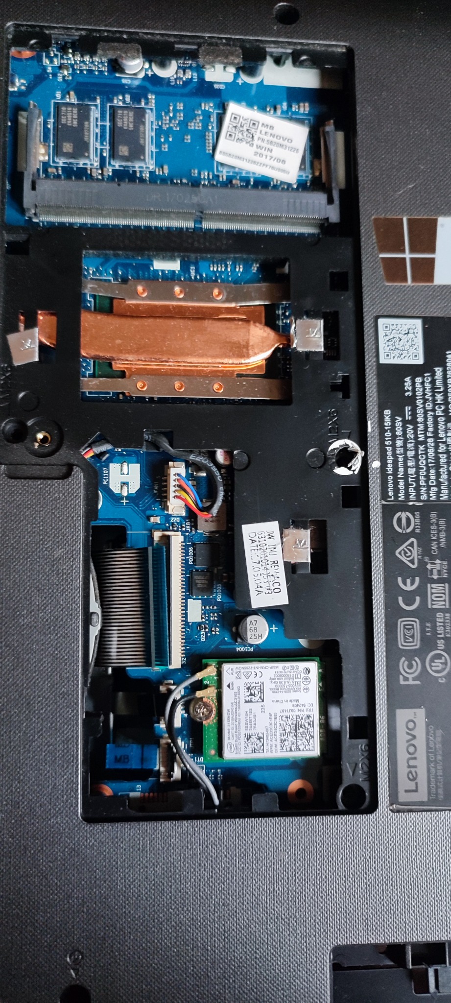Wnętrze laptopa Lenovo z widoczną płytą główną, układem chłodzenia (miedziane radiatory), kartą sieciową Wi-Fi Intel 3165NGW oraz naklejkami z numerami seryjnymi i kodami QR.