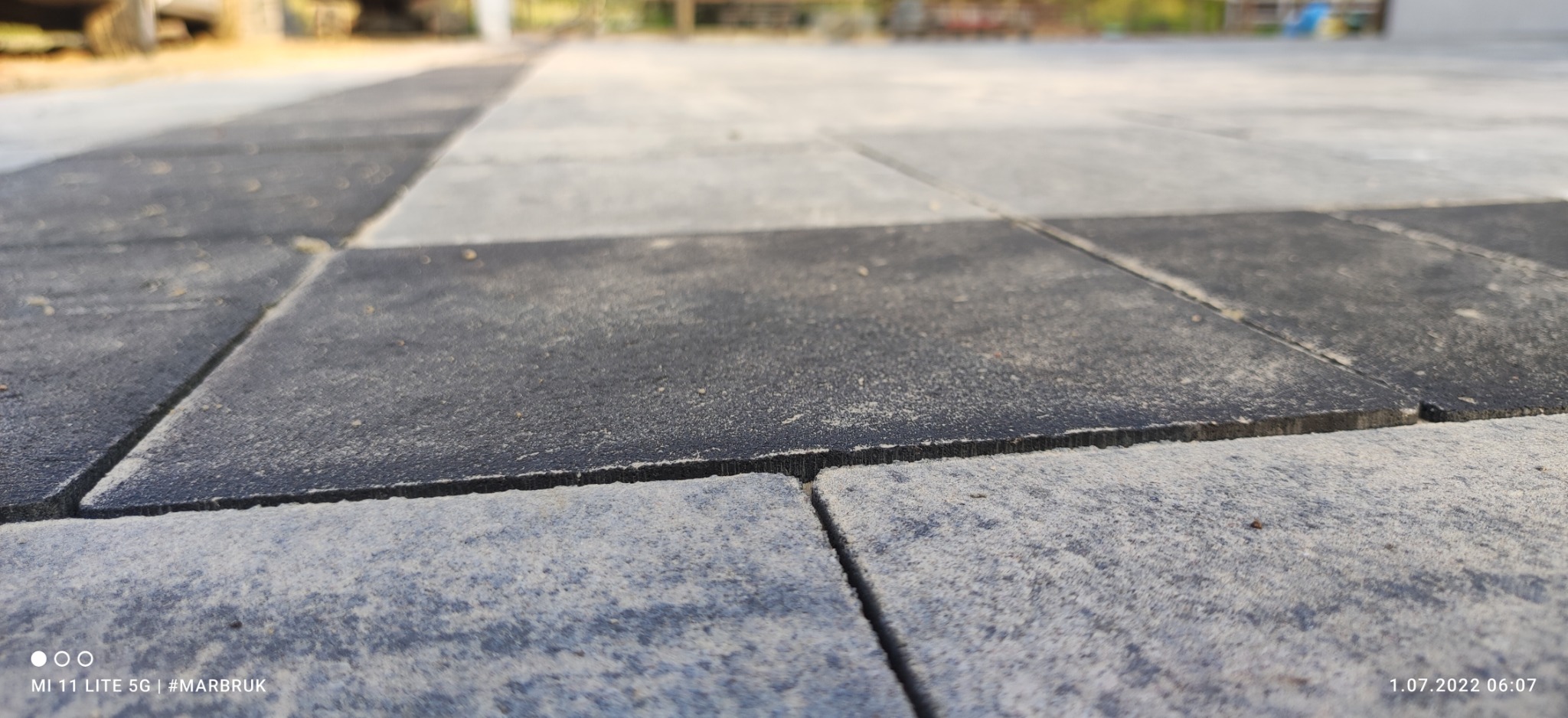 Szachownica z ułożonej kostki brukowej w odcieniach szarości, widoczna z niskiej perspektywy, z delikatnym rozmyciem tła.