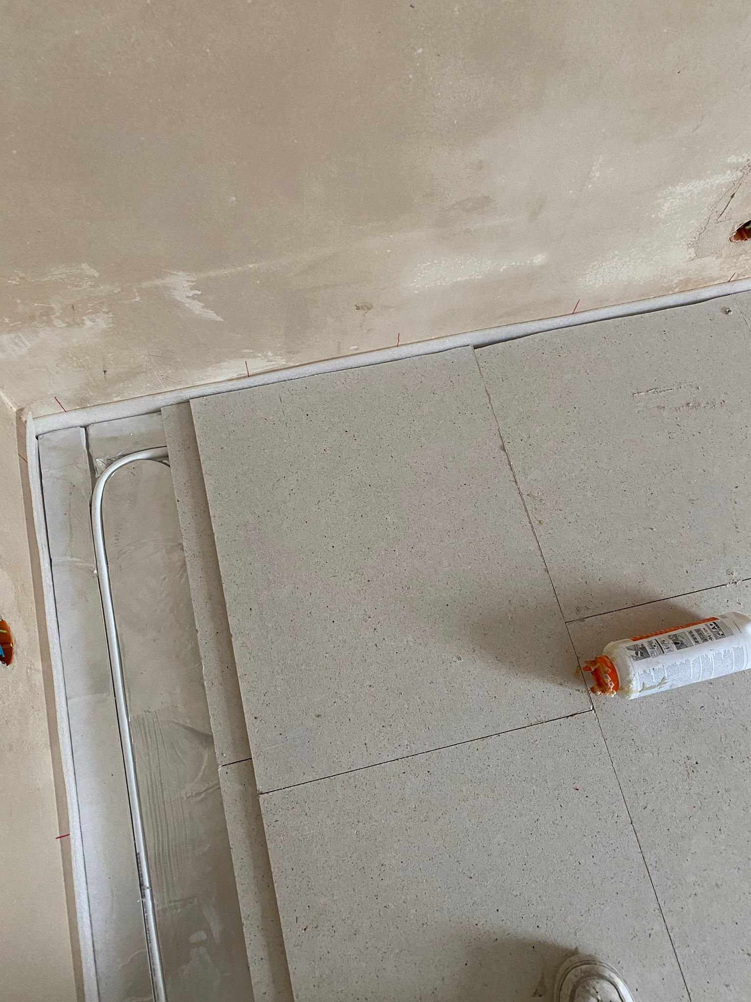 Fragment podłogi w trakcie montażu ogrzewania podłogowego: widoczne rurki grzewcze, płyty izolacyjne i tuba z klejem/uszczelniaczem, surowy stan ścian