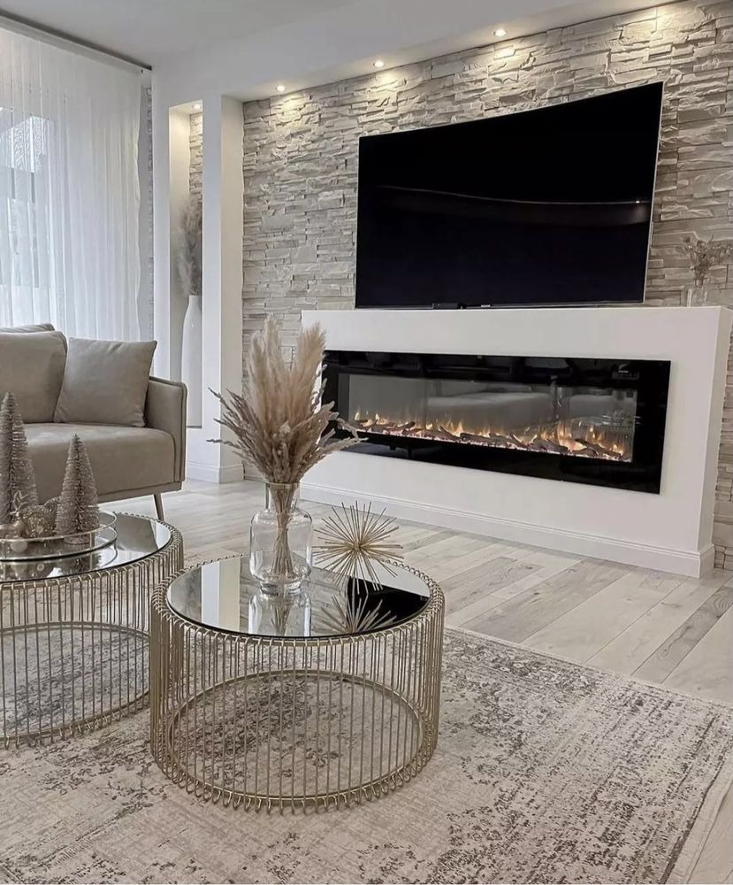 Elegancki salon z kamienną ścianą, telewizorem nad nowoczesnym kominkiem elektrycznym, okrągłe stoliki kawowe z metalową konstrukcją i szklanym blatem.