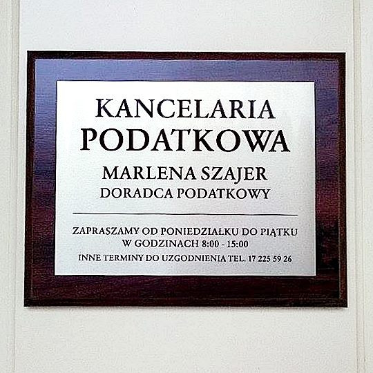 Tabliczka informacyjna Kancelarii Podatkowej Marlena Szajer, doradca podatkowy, godziny otwarcia od poniedziałku do piątku 8:00-15:00, kontakt telefoniczny.