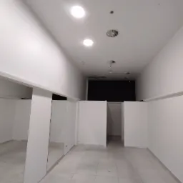 Wnętrze pustego, nowo wykończonego lokalu usługowego z białymi ścianami, jasnymi płytkami podłogowymi i wnękami oddzielonymi białymi ściankami działowymi.