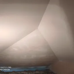 Poddasze z ukośnym sufitem po nałożeniu gładzi, widoczne łączenia płyt gipsowych i fragment podłogi z resztkami materiałów budowlanych.