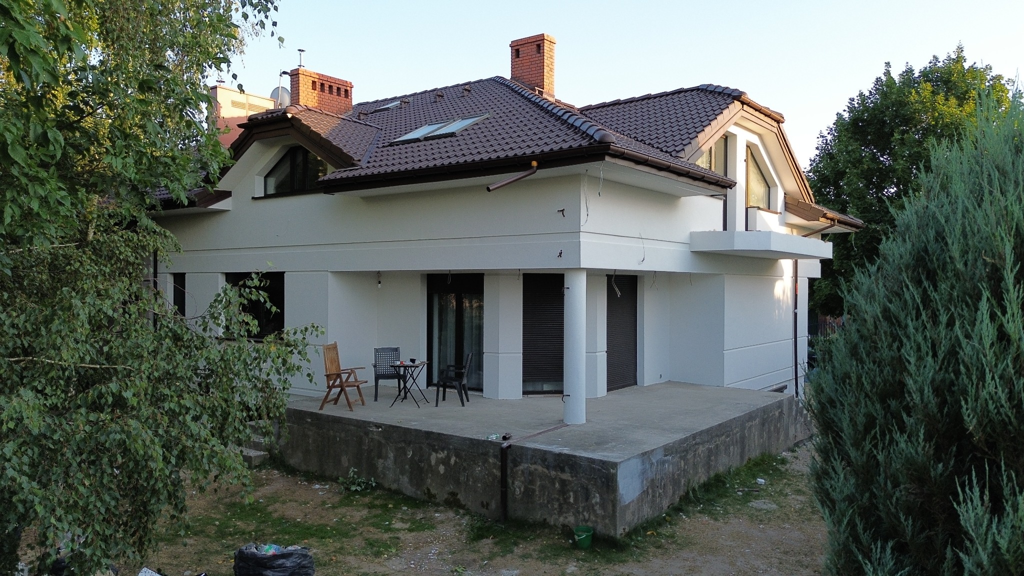 Biały dom jednorodzinny z brązowym dachem, widoczny z poziomu gruntu, z elementami wykończeniowymi i tarasem. Uwagę zwraca nowoczesna bryła budynku.