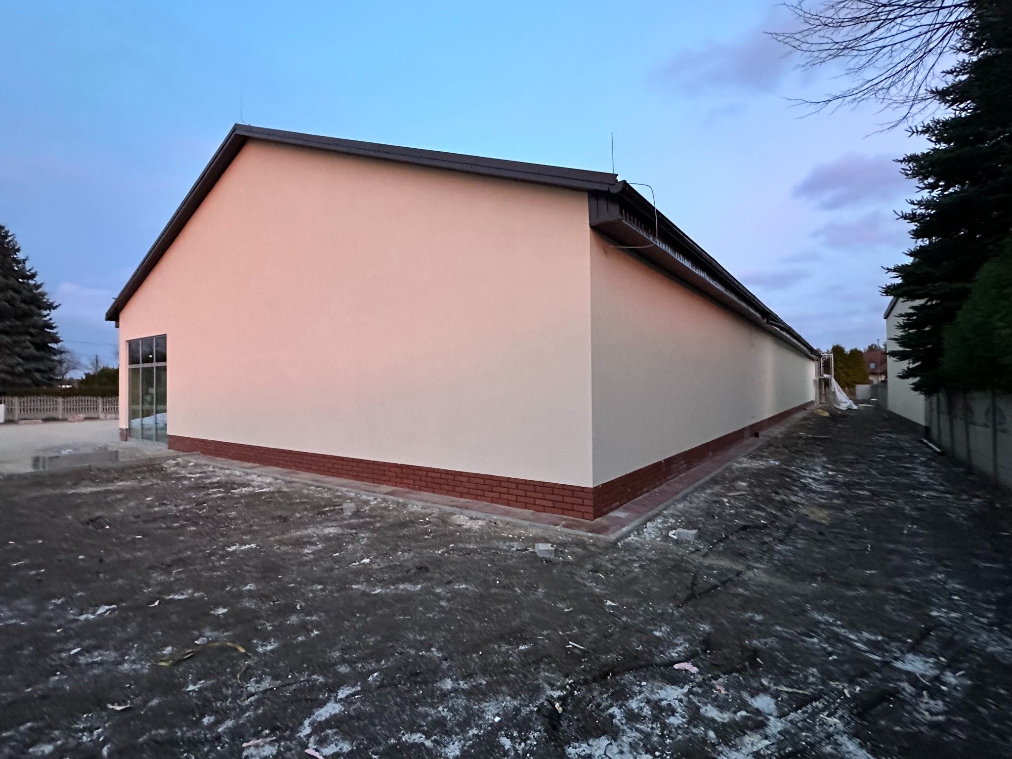 Budynek po renowacji elewacji z nową, jasną fasadą i czerwoną ceglaną podmurówką, sfotografowany z niskiego kąta przy pochmurnym niebie.