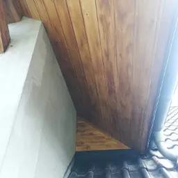 Wykończone drewnem poddasze z widocznym ociepleniem, fragmentem dachu pokrytego dachówką i rynną spustową