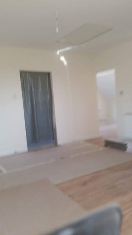 Przygotowane pomieszczenie do malowania: zabezpieczone folią drzwi, częściowo zakryta podłoga, widoczny fragment sufitu z otworem.