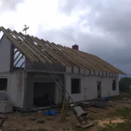 Surowy stan budynku z pustaków z drewnianą konstrukcją dachu w trakcie budowy, widoczne narzędzia i materiały budowlane.