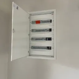 Otwarta, biała skrzynka rozdzielcza z bezpiecznikami na ścianie. Widoczne cztery rzędy bezpieczników. Skrzynka marki ETI.