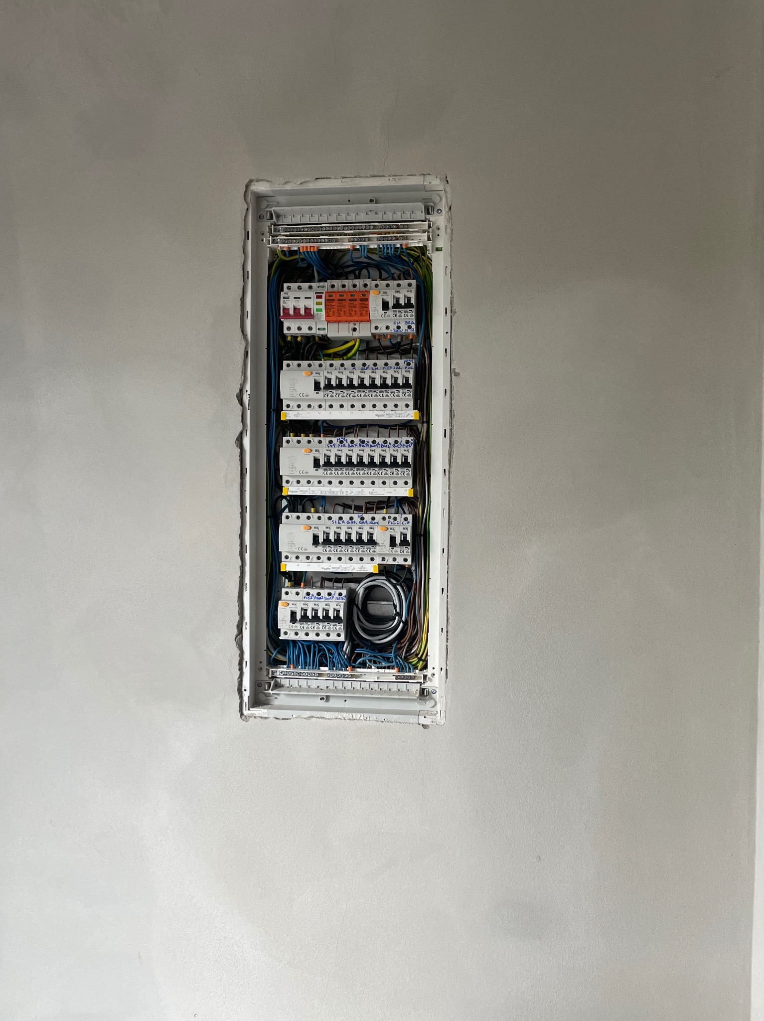 Rozdzielnica elektryczna z bezpiecznikami i okablowaniem, zamontowana w ścianie, gotowa do dalszych prac wykończeniowych. Widoczne kable i listwy montażowe.