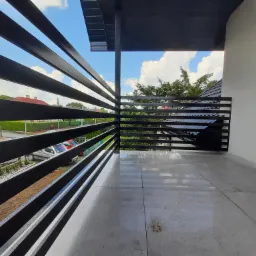 Nowoczesna, czarna balustrada balkonowa z metalowymi poziomymi prętami, widok na okolicę z fragmentem nieba i drzew, szara płytka podłogowa.