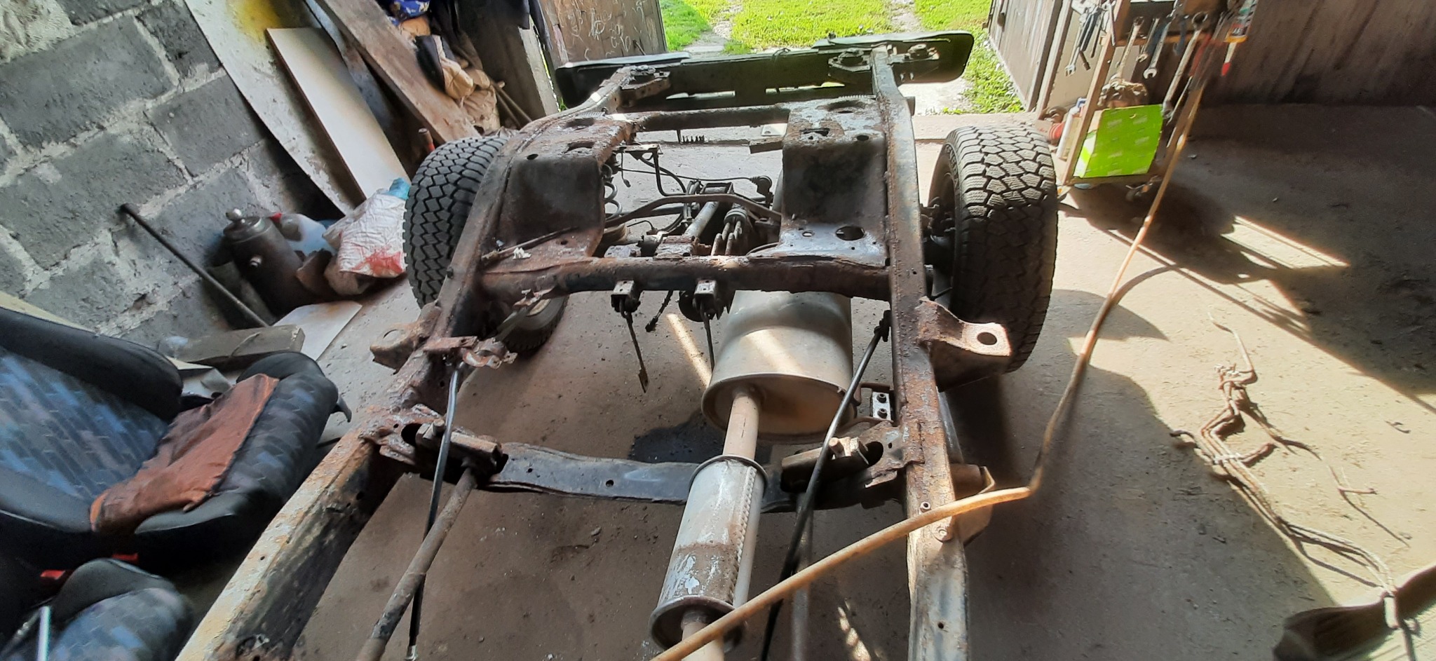 Zardzewiała rama samochodu terenowego z widocznymi elementami zawieszenia i układu wydechowego, częściowo zdemontowana, w warsztacie.