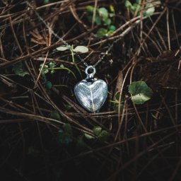 CoZaFoto - Srebrny wisiorek w kształcie serca z delikatnym wzorem żyłek, leżący na ściółce z brązowych igieł sosnowych i drobnych zielonych listków.