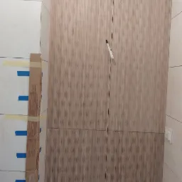 Montaż drewnopodobnej zabudowy w łazience z widocznymi przyłączami wodnymi i zabezpieczonymi płytkami.