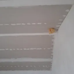 Sufit z płyt kartonowo-gipsowych, widoczne łączenia i miejsca po wkrętach, fragment izolacji w rogu.