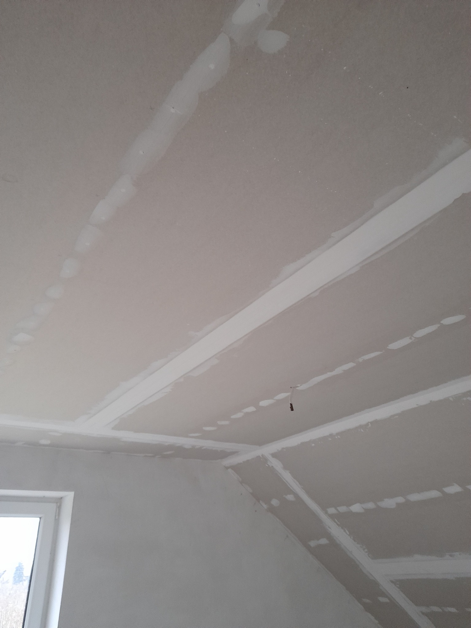 Sufit z płyt kartonowo-gipsowych w trakcie szpachlowania łączeń, widoczne paski szpachli i niewielki zwisający kabel.