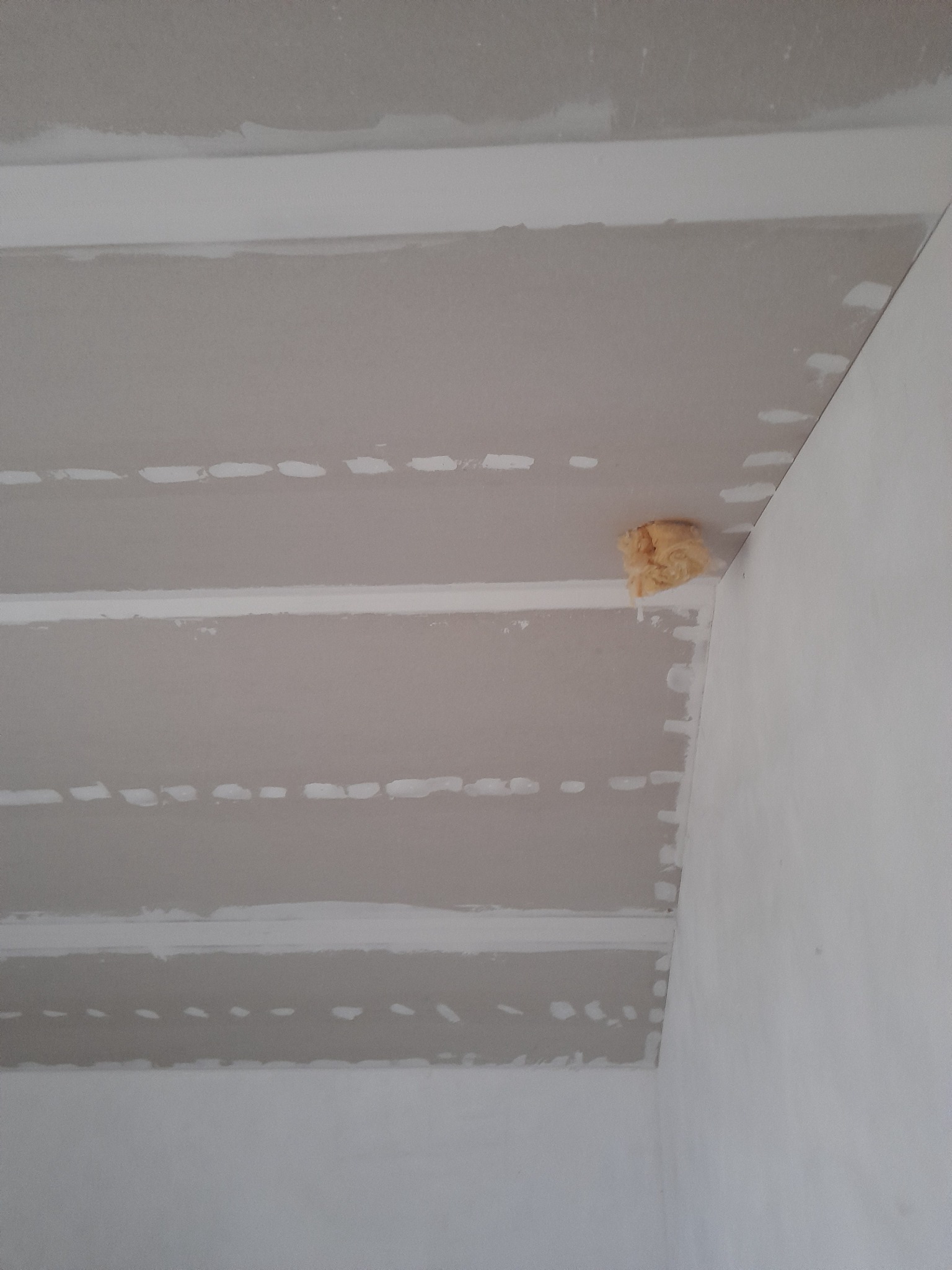 Sufit z płyt kartonowo-gipsowych, widoczne łączenia i miejsca po wkrętach, fragment izolacji w rogu.