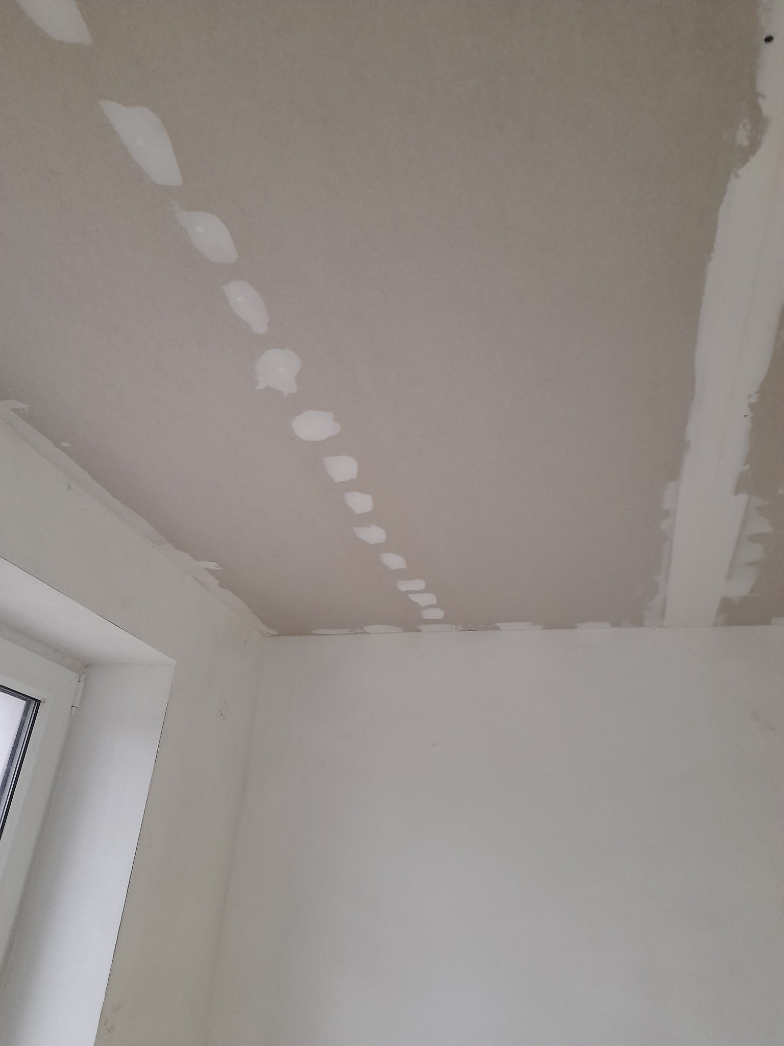 Płyta gipsowo-kartonowa na suficie z widocznymi miejscami po wkrętach wypełnionymi szpachlą, przygotowana do dalszej obróbki.