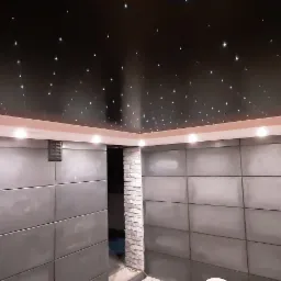 Wykończona łazienka z panelami ściennymi w odcieniach szarości i sufitem imitującym rozgwieżdżone niebo, oświetlonym punktowymi lampami.