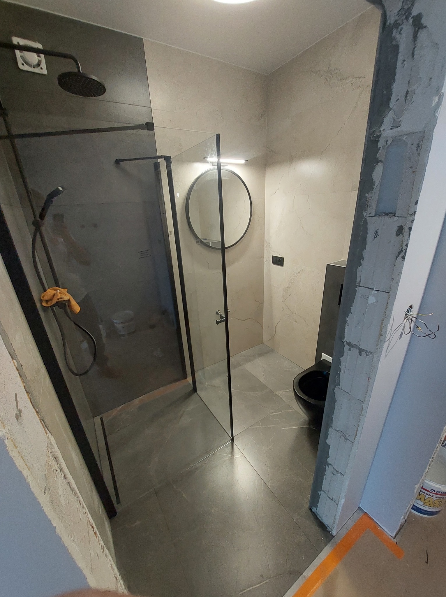 Wykończona łazienka w Wołominie z kabiną typu walk-in z czarnymi profilami, okrągłym lustrem z podświetleniem i podwieszaną toaletą w nowoczesnym stylu.