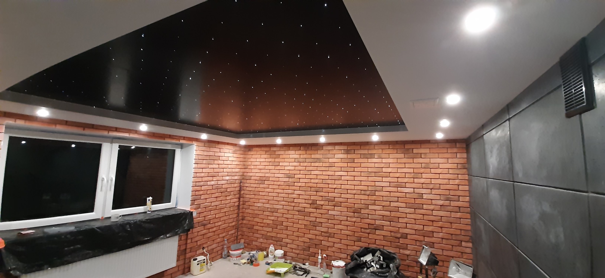 Pokój po remoncie: ściana z cegły, sufit imitujący nocne niebo z gwiazdami, szara ściana z panelami. Widoczne ślady po pracach wykończeniowych.