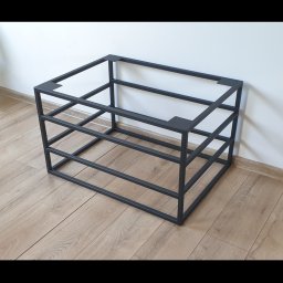 Faktoria Kamienia Grudzień Monika Juda - Czarna, spawana konstrukcja stalowa w kształcie sześcianu, z trzema poziomami, umieszczona na podłodze z paneli, na tle białej ściany, z widocznymi spawami w narożnikach.