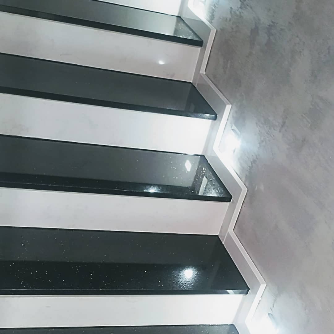 Nowoczesne schody z czarnymi stopniami z połyskującego kamienia, białe podstopnice i szara ściana o fakturze betonu.