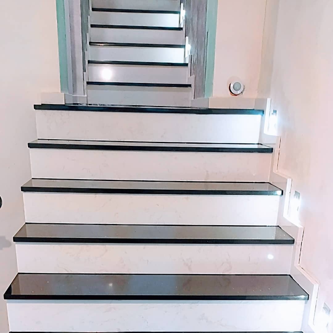 Nowoczesne schody wewnętrzne z białymi stopnicami i czarnymi krawędziami, podświetlane punktowymi lampkami w ścianie, widok z dołu.