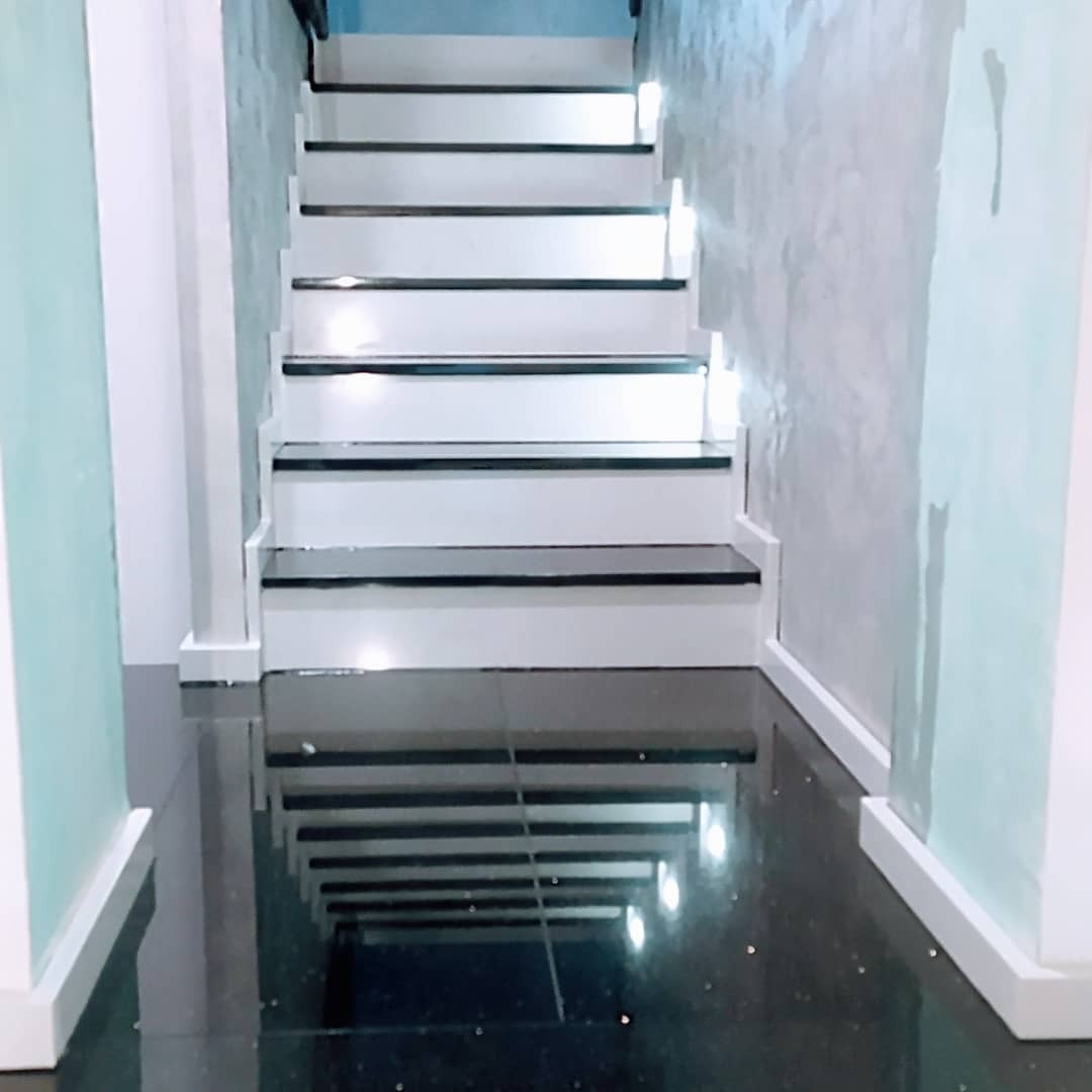 Białe schody z czarnymi akcentami i błyszczącą podłogą, widok z dołu, oświetlenie punktowe