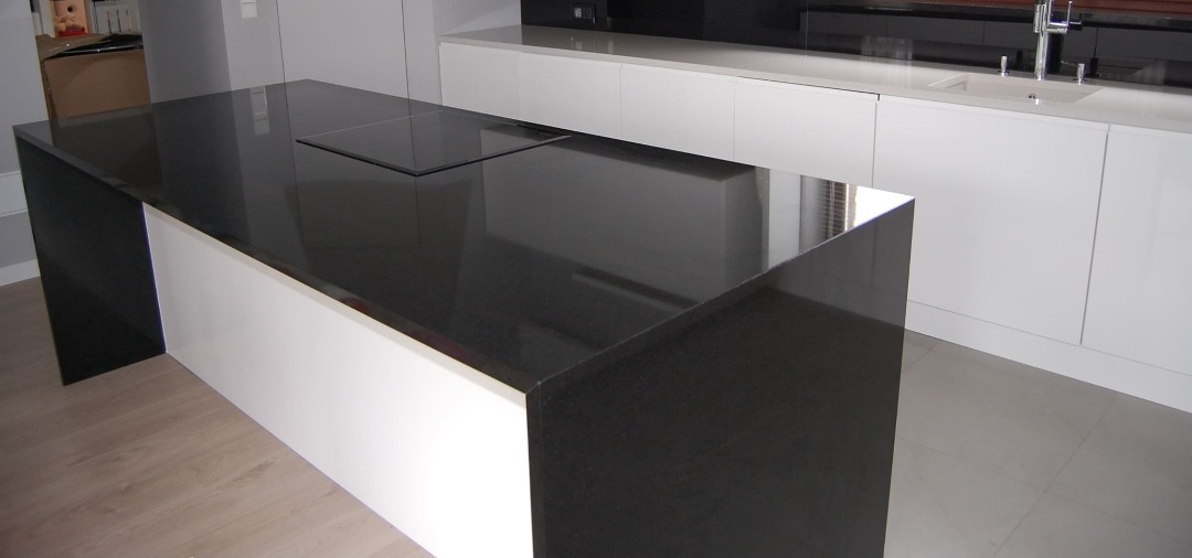 Czarny, błyszczący blat z kamienia z wbudowaną płytą grzewczą, zamontowany w nowoczesnej kuchni w Alwerni. Minimalistyczny design z białymi szafkami w tle.