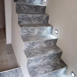 Schody wewnętrzne wyłożone szarą mozaiką z nieregularnych kamieni, oświetlone małymi, kwadratowymi lampkami w ścianie.