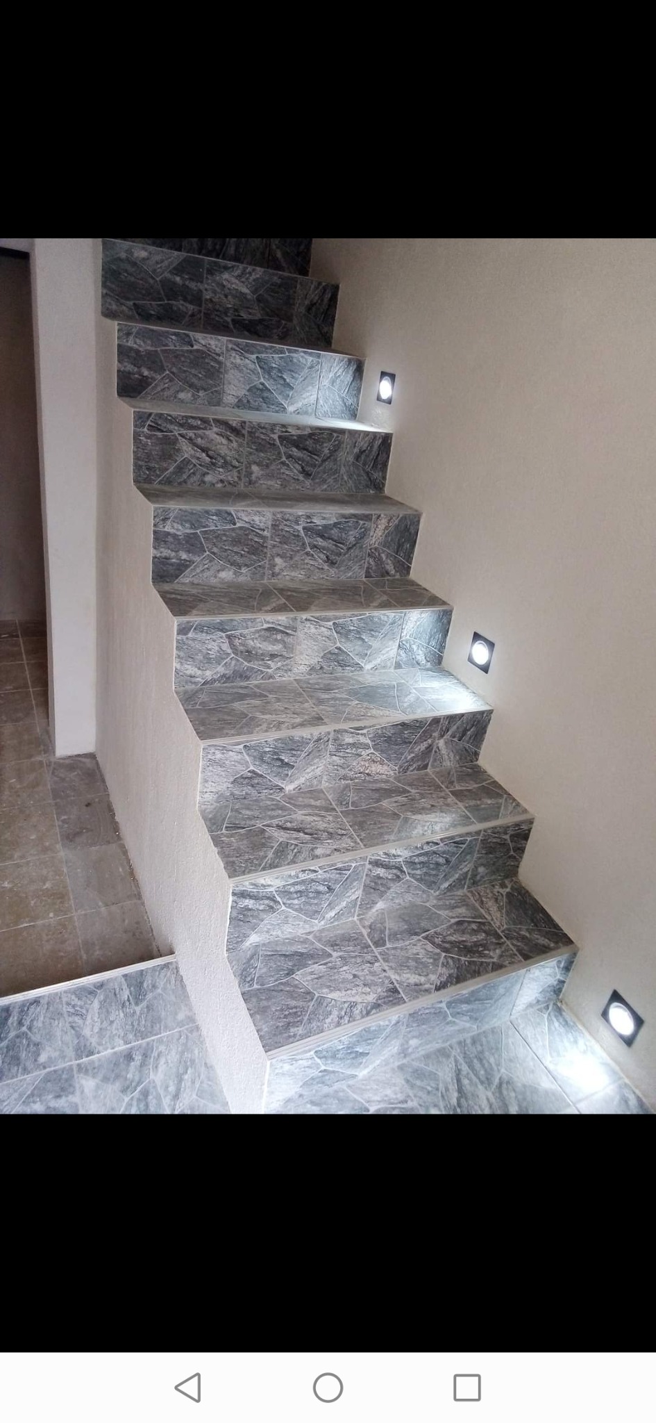 Schody wewnętrzne wyłożone szarą mozaiką z nieregularnych kamieni, oświetlone małymi, kwadratowymi lampkami w ścianie.