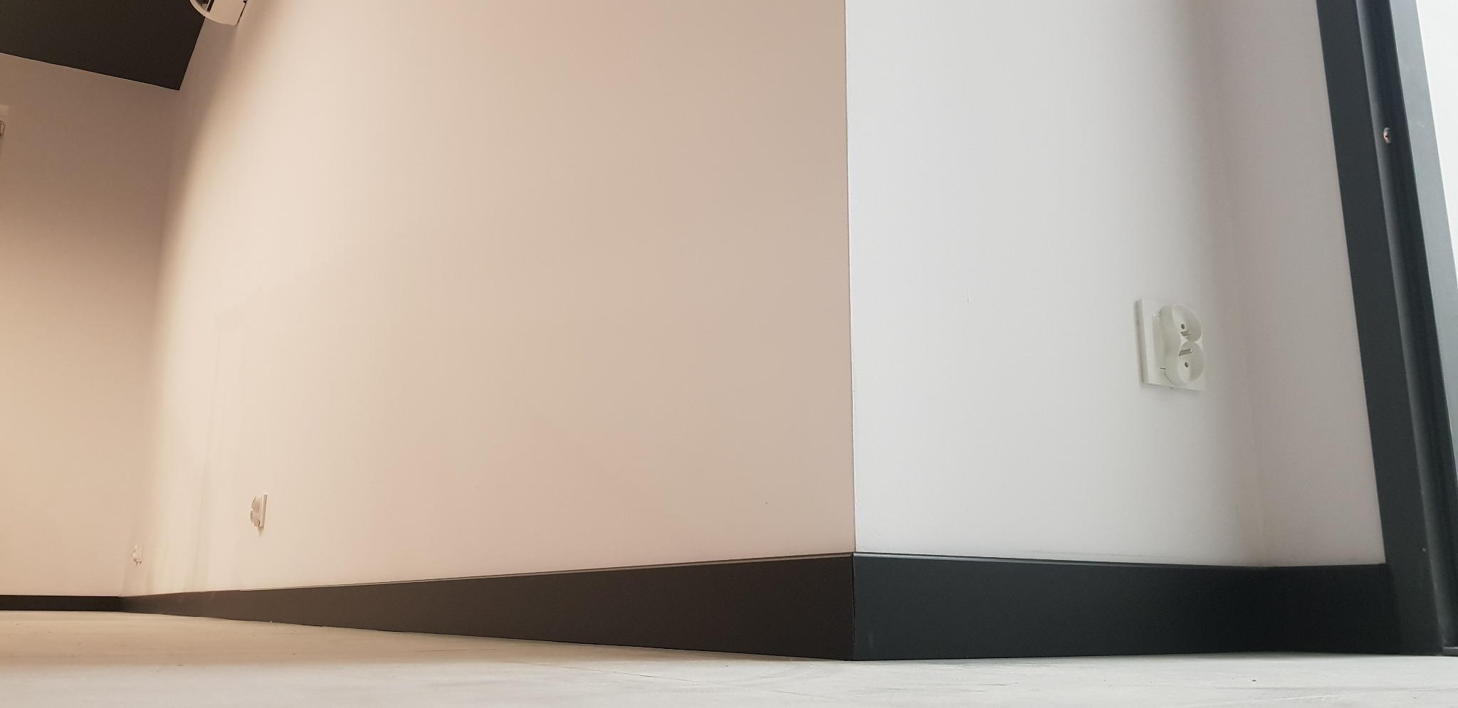 Wnętrze po remoncie: Ściany pomalowane na biało, z czarnymi listwami przypodłogowymi i gniazdkiem elektrycznym na ścianie.