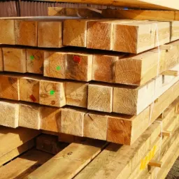 Stos drewnianych belek o przekroju kwadratowym, spiętych sznurkiem, z widocznymi oznaczeniami kolorowymi markerami na niektórych końcach.