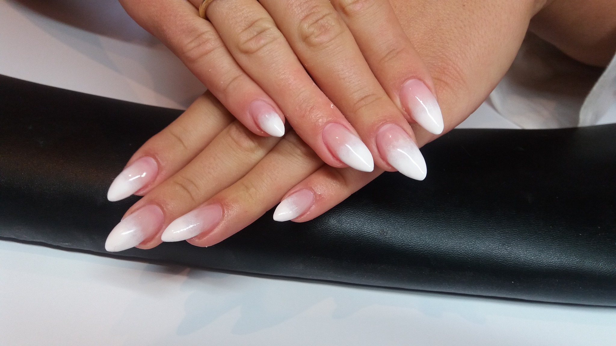 Dłonie z białym ombre na długich, szpiczastych paznokciach, złoty pierścionek na palcu.