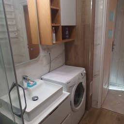 SAN-REMOnt - Nowoczesna łazienka z umywalką nablatową, pralką Candy i drewnianymi szafkami. Lustro z podświetleniem LED. Płytki imitujące drewno na ścianie.