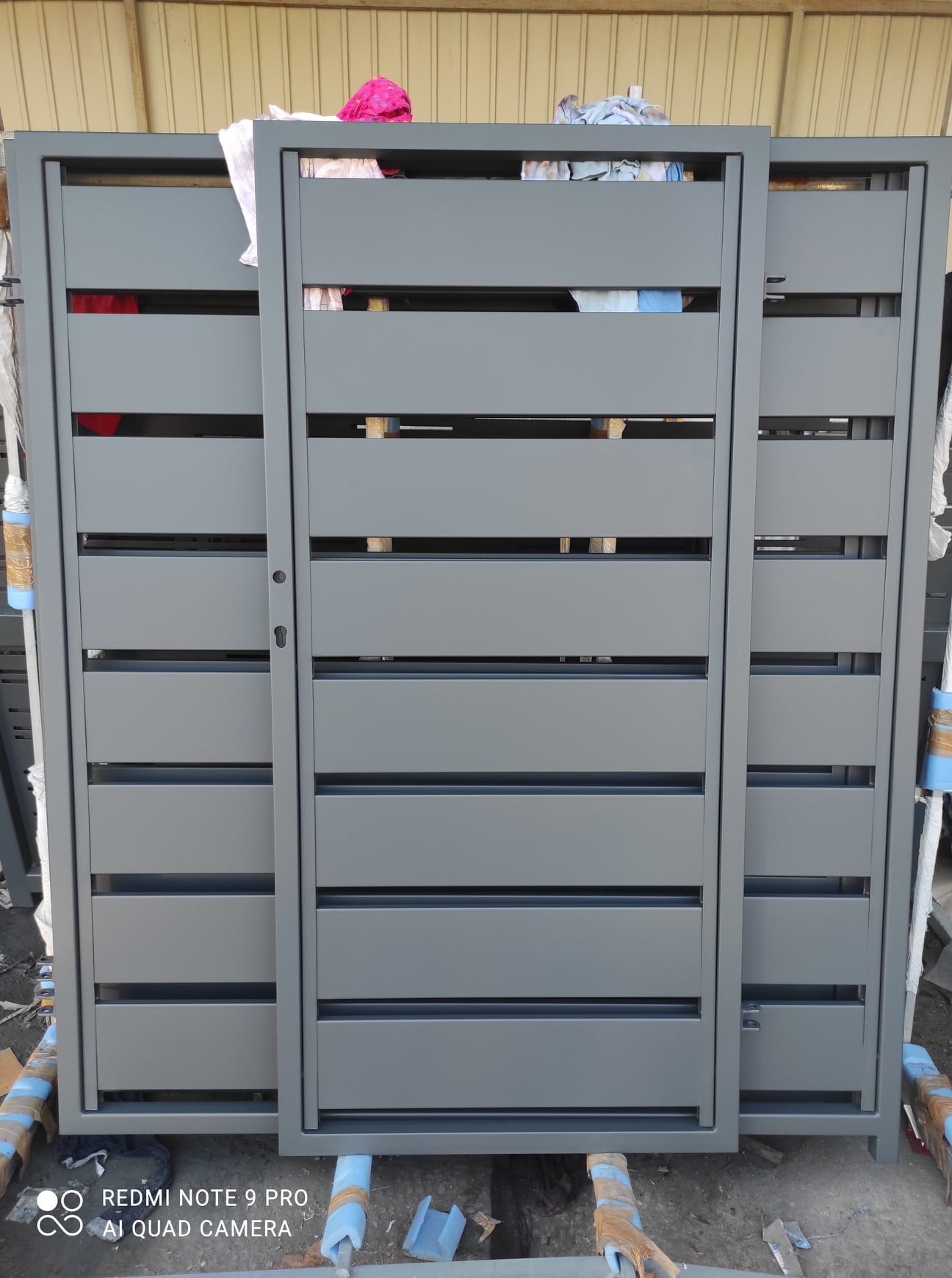 Nowoczesna, szara brama przesuwna z poziomymi panelami, widoczna w trakcie produkcji lub składowania, z elementami zabezpieczającymi narożniki.