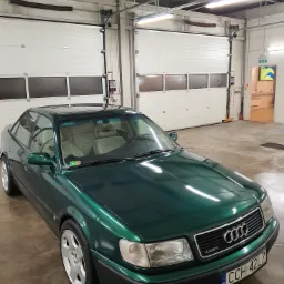 Zielony samochód Audi Quattro, model z lat 90-tych, zaparkowany w jasnym pomieszczeniu z dwoma bramami garażowymi, z widoczną tablicą rejestracyjną CCH 42L7.