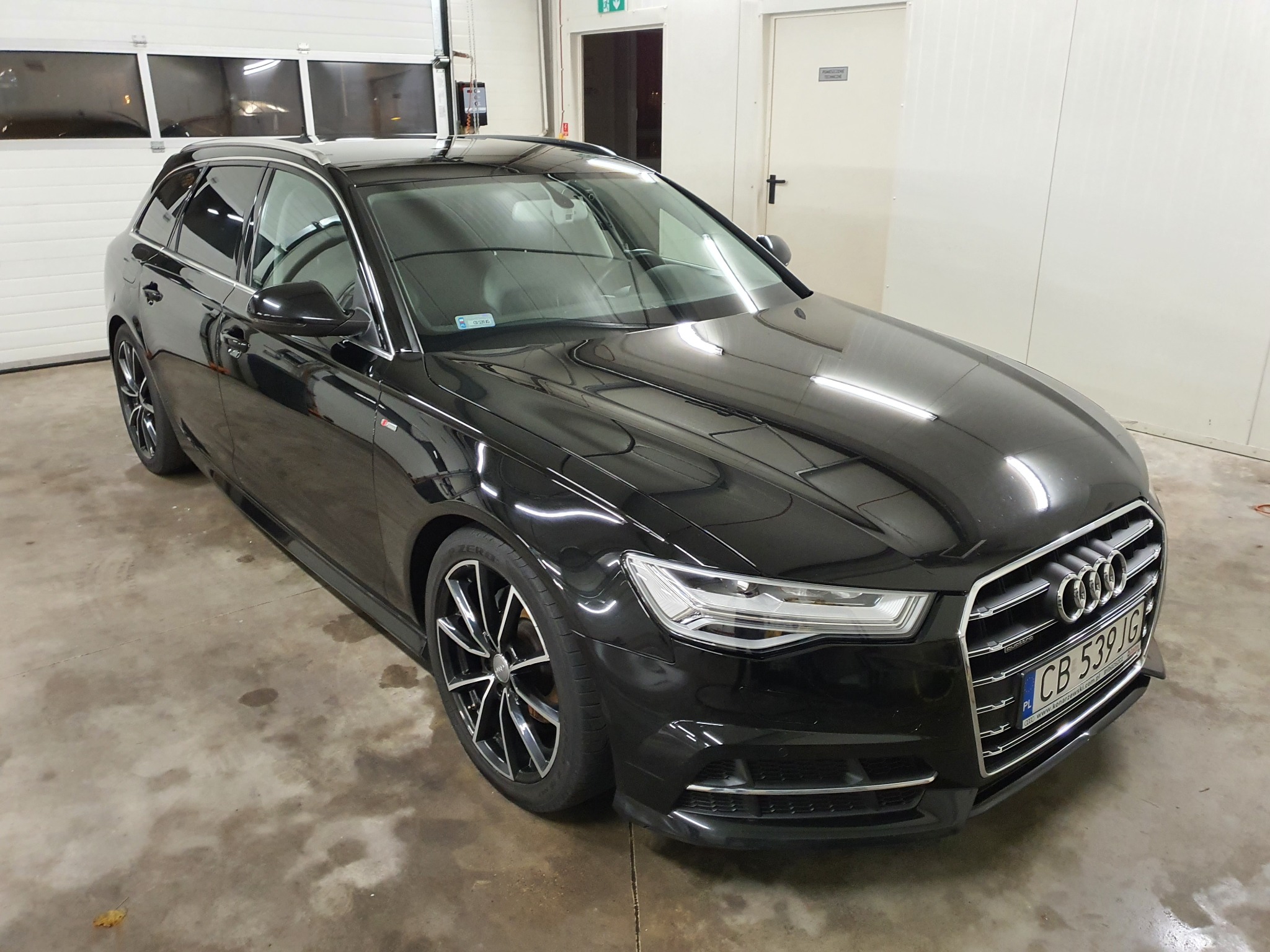 Błyszczący czarny samochód kombi marki Audi po umyciu, stojący w jasnym garażu z betonową podłogą.