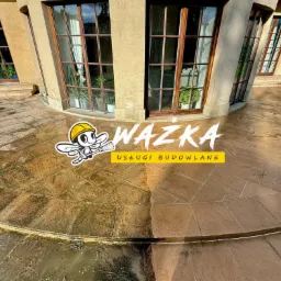 Częściowo umyta, brązowa, kamienna elewacja budynku z dużymi oknami, widoczny efekt czyszczenia, logo firmy budowlanej w centralnej części kadru.