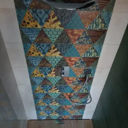 Nowoczesna kabina prysznicowa z deszczownicą i baterią podtynkową, wykończona mozaiką z trójkątnych płytek w odcieniach brązu, niebieskiego i zieleni, z drewnopodobną podłogą.