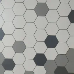 Ściana wyłożona heksagonalnymi płytkami w odcieniach bieli, szarości i grafitu, z widocznymi fugami.