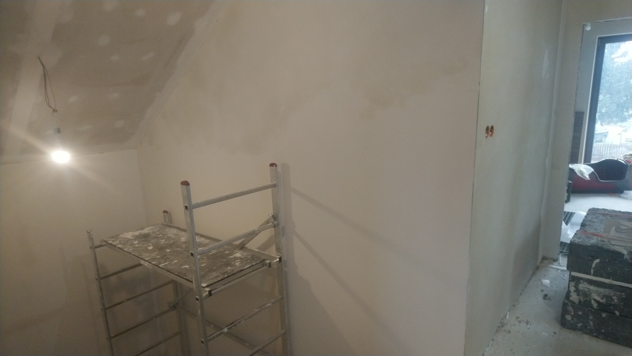 Wnętrze pokoju w trakcie prac wykończeniowych w Oleśnicy, widoczne ściany po nałożeniu warstwy wygładzającej, aluminiowy ruszt oraz sufit ze śladami po szpachlowaniu.