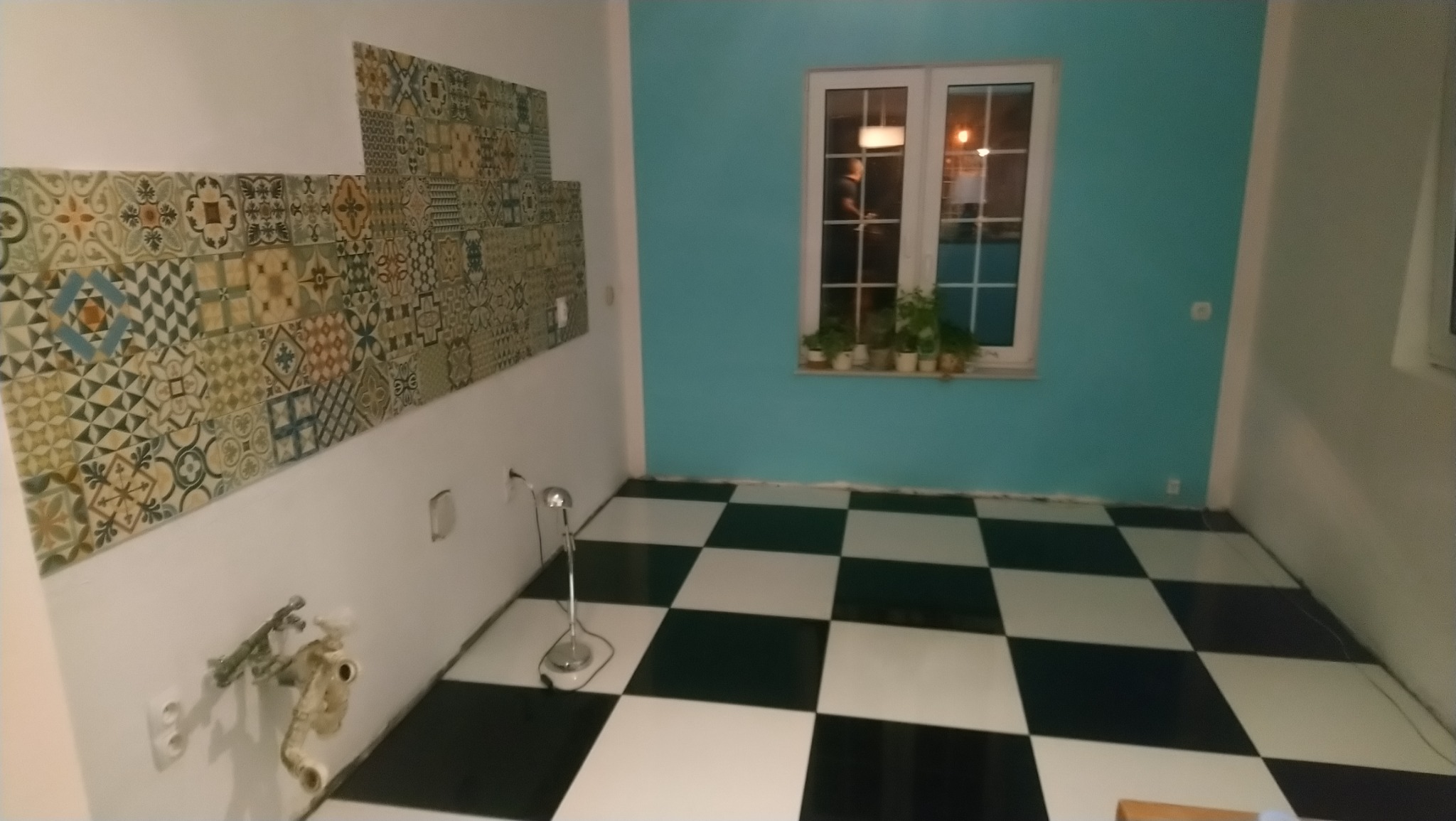 Niedokończona ściana z dekoracyjnymi płytkami w kuchni z szachownicą na podłodze i turkusową ścianą z oknem.