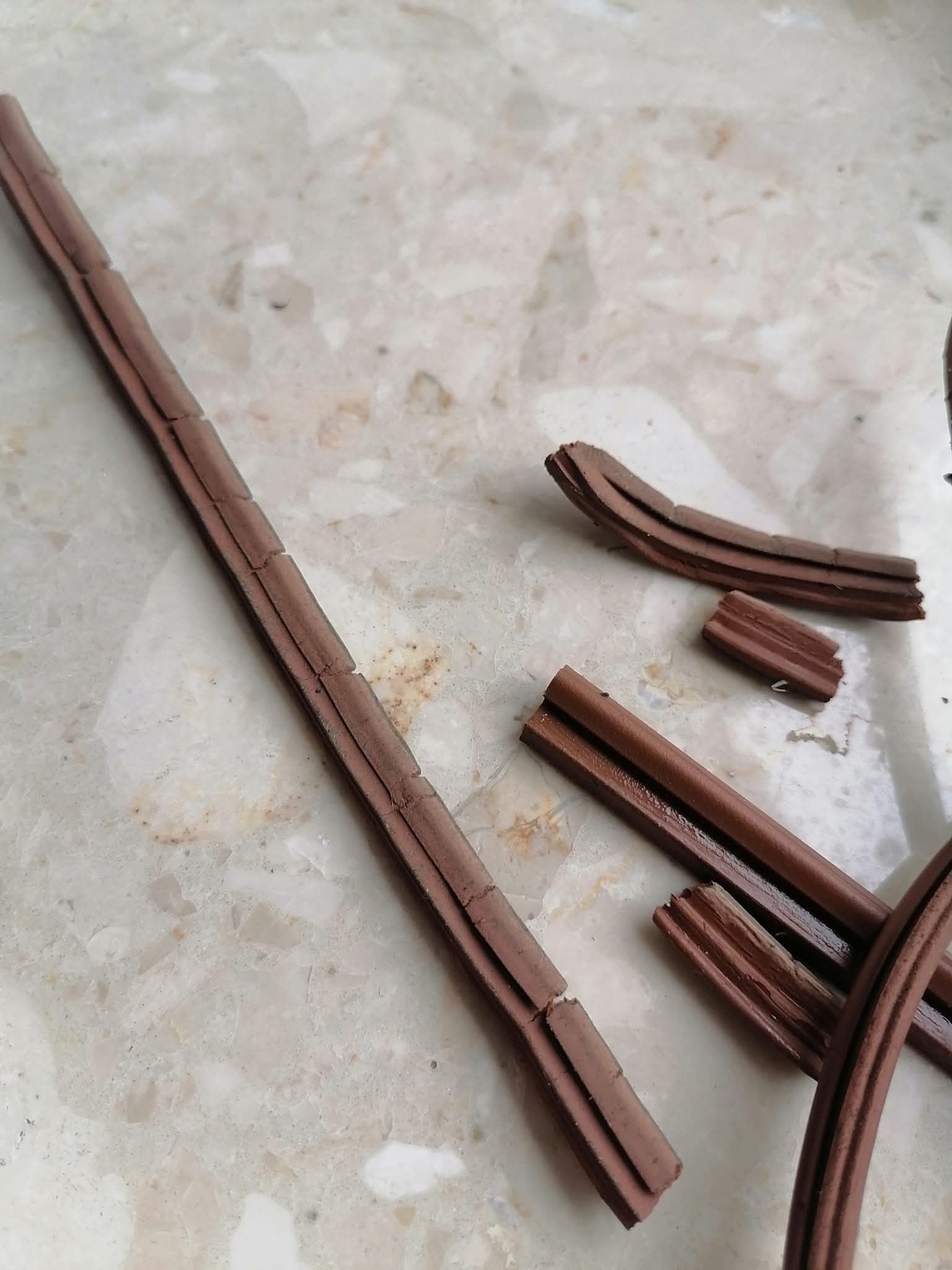 Uszczelka okienna brązowa, pęknięta, leżąca na marmurowym blacie. Widoczne fragmenty uszczelki o różnej długości i kształcie, sugerujące wymianę lub naprawę.